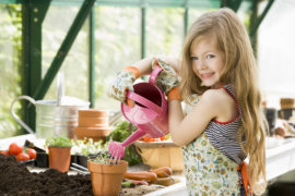 Young girl watering plants in greenhouse smiling